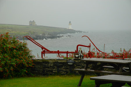 Picture of a view over a rain wet garden towards a lighthouse in the rain, grey clouds behind it