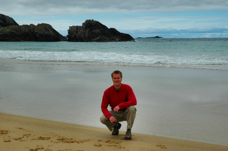 Picture of a person kneeling on the sand in a bay, the sea in the background (Lossit Bay, Islay