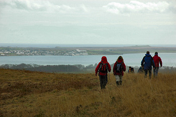 Picture of walkers descending a hill, a sea loch and a village in the distance