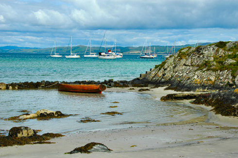 Picture of a beach with a rowing boat and a few sailing yachts moored out at sea