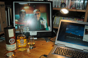 Picture of a whisky being poured seen on a monitor, a bottle and a glass standing in front of it