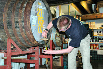 Picture of a man filling a whisky bottle from the cask, using a valinch