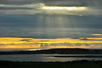 Picture of a sunset on a partly cloudy sky, the sea in the background, a loch (lake) in the foreground