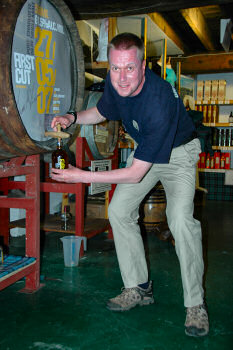 Picture of a man filling a whisky bottle from a cask using a valinch