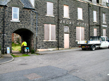 Picture of the old Islay Hotel with a biker cycling through the arch next to it
