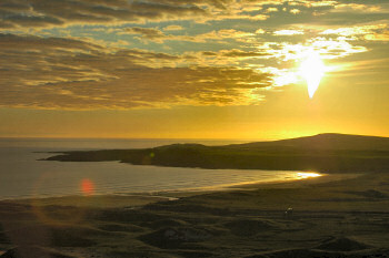 Picture of a sunset over a low hill near a bay on Islay
