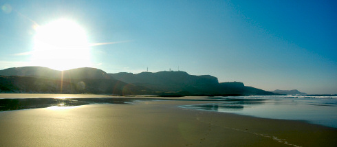 Picture of a beautiful sunrise over a beach flanked by high crags and dunes