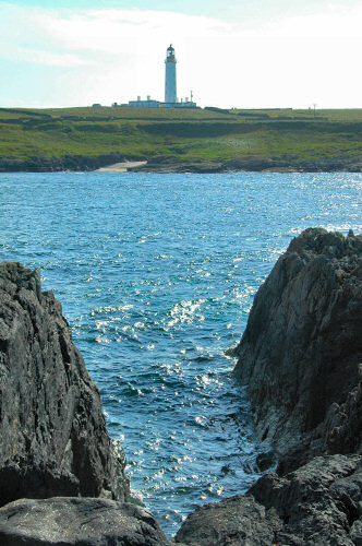 Picture of a lighthouse on the other side of a small sound, a rocky shore in the foreground