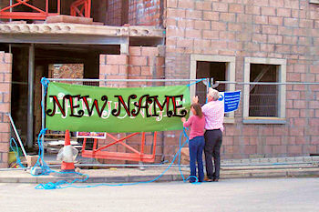 Picture of two people hanging up a sign reading 'new name'