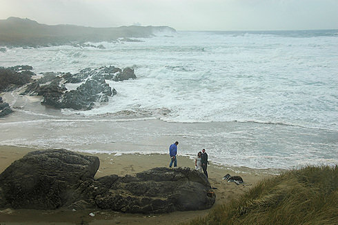 Picture of a beach at a bay with wild sea, a newlywed couple and a photographer in the foreground