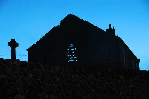 Picture of the ruin of a church and a Celtic cross next to it in the last evening light