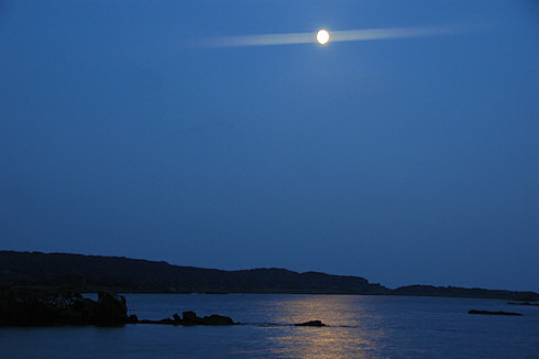 Picture of a full moon over a calm bay, the light of the moon reflecting on the water