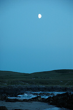 Picture of a partial moon over a coastal landscape