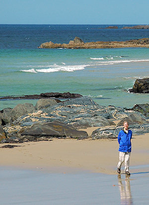 Picture of a woman walking on a beach with rocks in the background