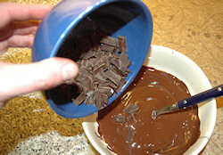 Picture of melted chocolate in a bowl with more chocolate being added
