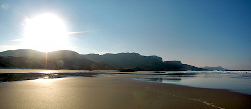 Picture of a sun rising above crags towering over a beach