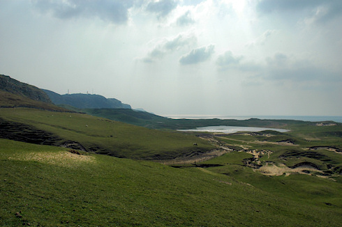 Picture of dunes and cliffs along a wide bay, hazy sun breaking through clouds