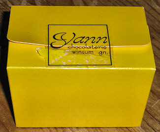 Picture of a small yellow cardbox box with a label Yann chocolaterie winsum