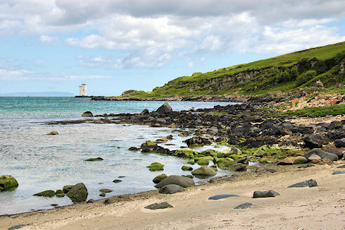 Picture of a lighthouse on a rocky outcrop, seen along a rocky shoreline from a beach