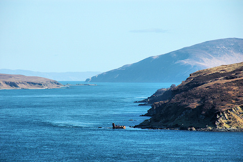 Picture of a view down a sound between two islands, a distillery in the foreground and a lighthouse in the distance