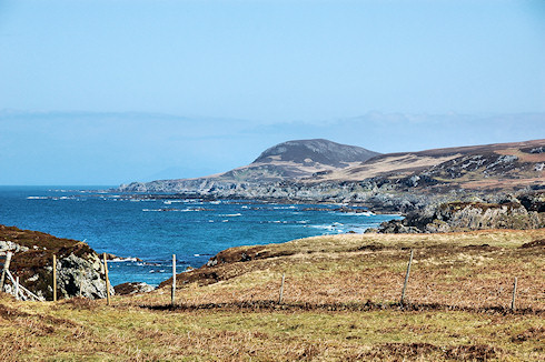 Picture of a view along a wild coastline, various low cliffs and a conical shaped hill at the end