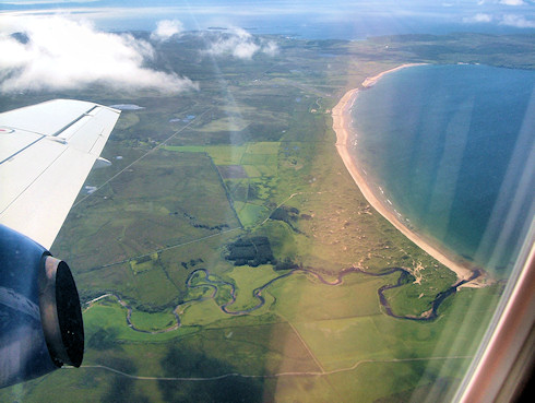 Picture of a wide bay with sandy beach, taken from a plane. A river at the bottom of the picture