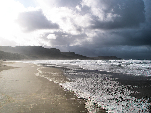 Picture of a bay on a stormy day, bright sun on one side over the beach, black clouds on the other side over the water