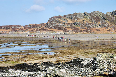 Picture of a large group of walkers crossing a beach between two islands at low tide