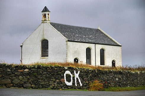 Picture of small church, in front of the church a stone wall with the letters 'OK' painted on it