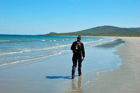 Picture of a woman walking along a long sandy beach, under a bright blue sunny sky