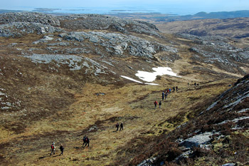 Picture of walkers in a small glen on a hill, some snow on the hillside