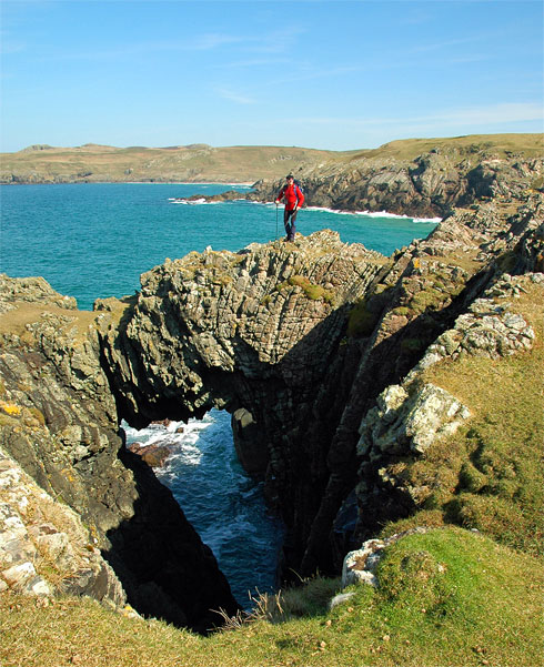 Picture of a walker standing on a natural arch above the sea