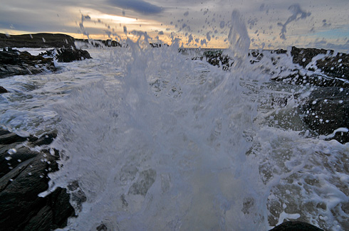 Picture of a wave breaking and splashing over rocks right in front of the lens