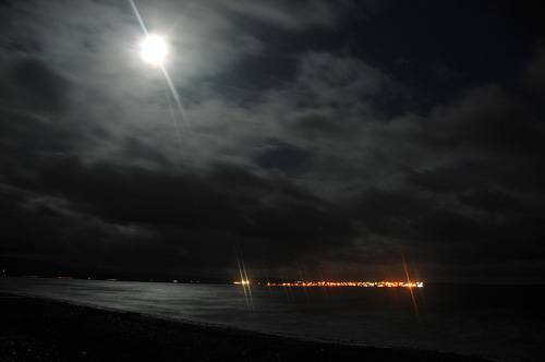 Picture of the Moon breaking through clouds to illumnate a sea loch, a village on the other side