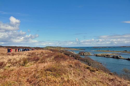 Picture of a group of walkers walking along a shoreline with small islands offshore