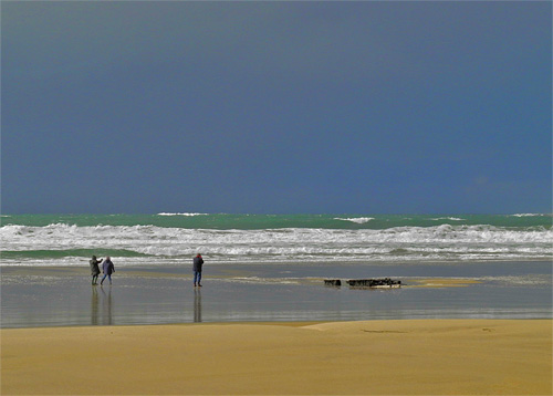 Picture of a beach with a wreck and three walkers under dark skies