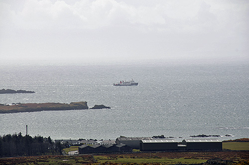 Picture of large distillery warehouses on a shore with a passing ferry