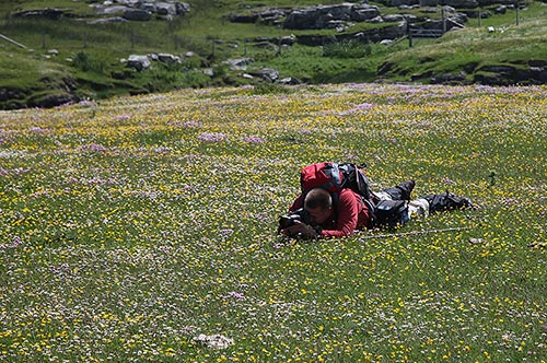 Picture of a man lying on the ground photographing the machair