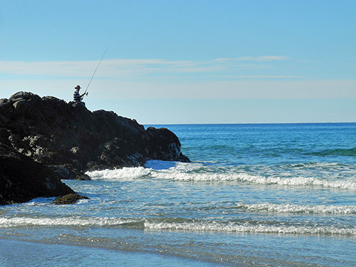 Picture of a man fishing from some rocks at the end of a bay