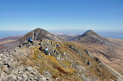 Picture of a few walkers on the top of a mountain, other mountains around